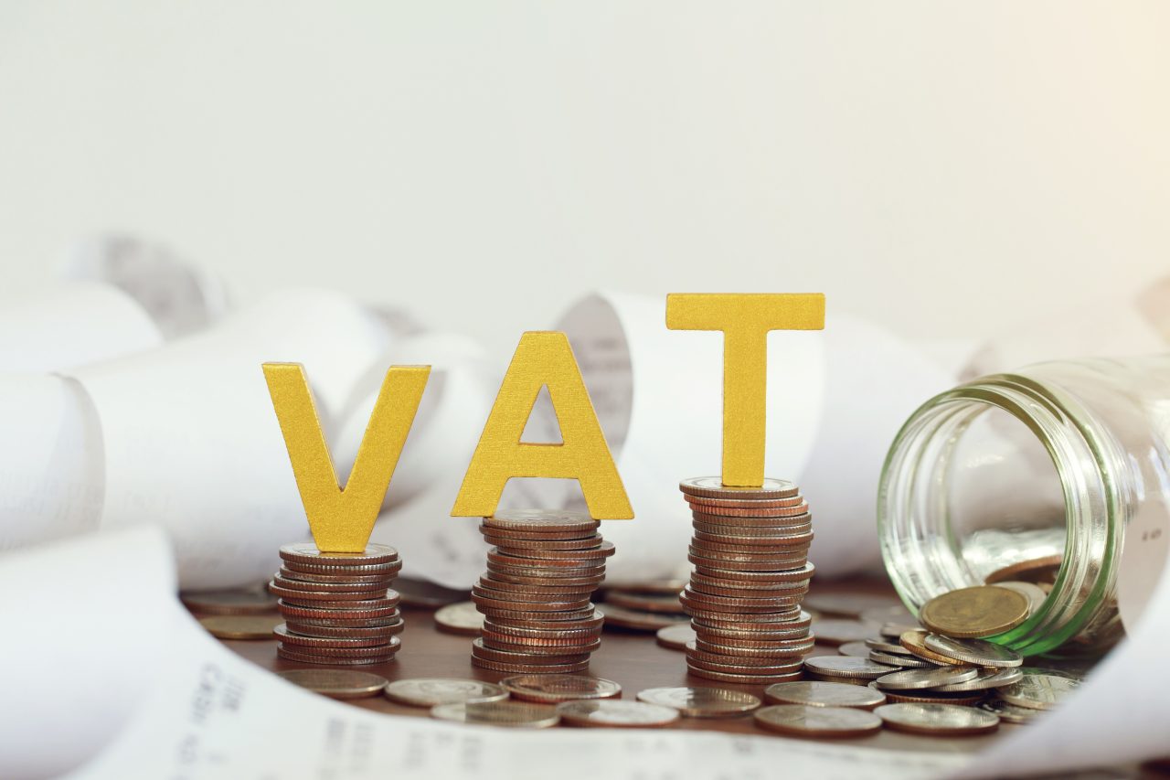 Vat Concept. Word vat put on stacked coins and glass bottles with coins inside on the wooden table. Vat time